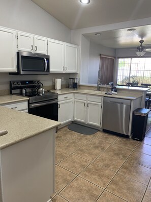 A kitchen with white cabinets, stainless steel appliances, a window with blinds, and a ceiling fan. - 3 King Beds, Heated Pool!! (Mesa)