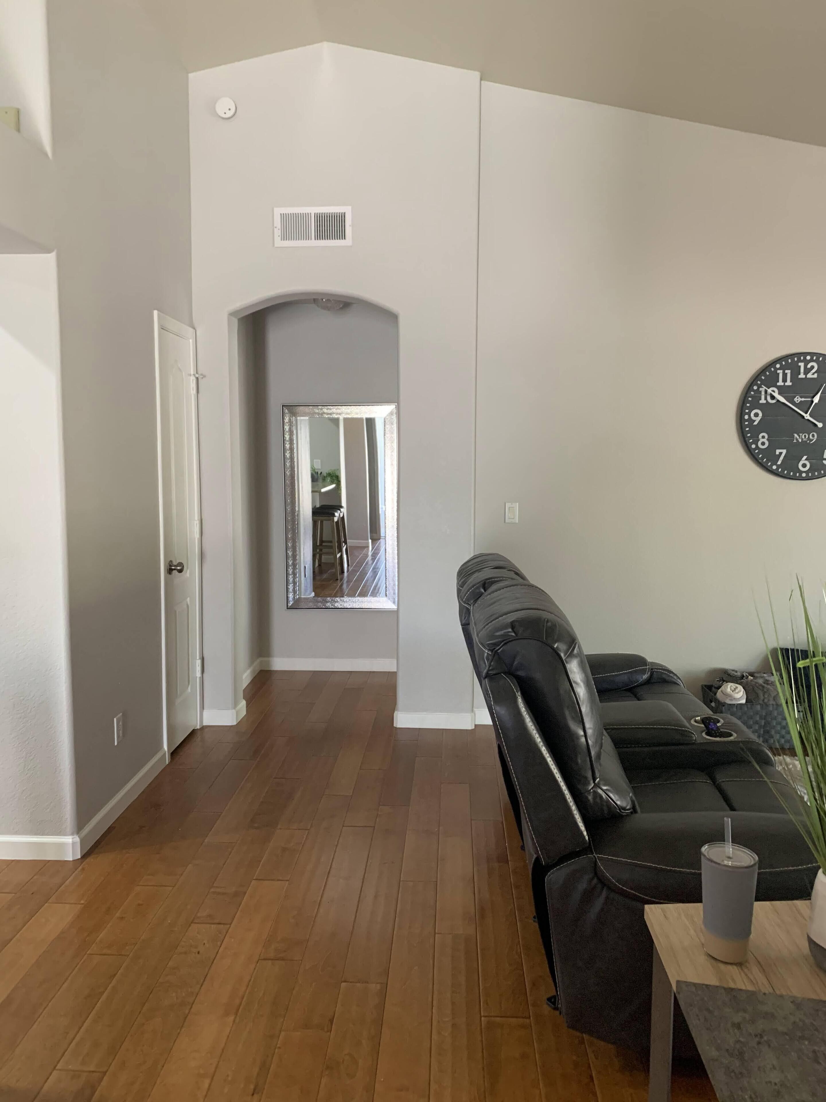 A modern living room with a black leather sofa, a wooden coffee table, and a wall clock.