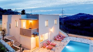 A modern two-story building with a pool and sun loungers.