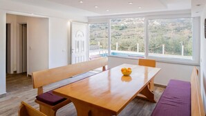A dining area with a wooden table, benches, and a view of a hilly landscape through large windows.