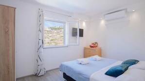 A bedroom with a bed, a dresser, a window with a view, and an air conditioning unit.