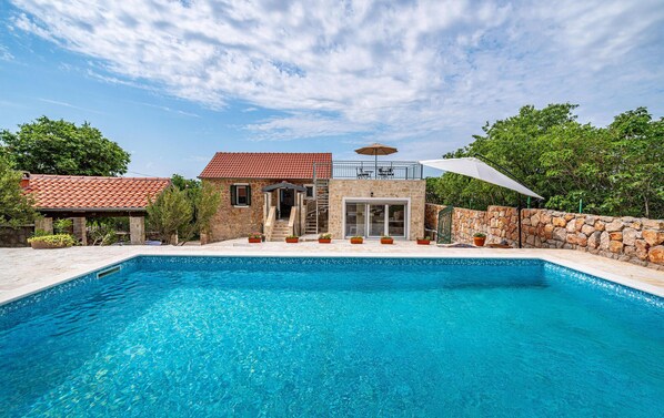 A swimming pool with a stone house and a covered patio area.