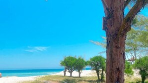 A hammock tied to a tree, overlooking a beach with a wooden fence and a clear blue sky. - Pé na areia. (Arraial do Cabo)