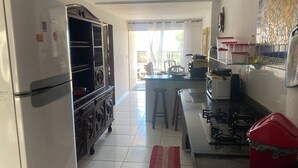 A kitchen with a refrigerator, stove, and microwave. There is a window with curtains, a tiled floor, and a red rug. - Pé na areia. (Arraial do Cabo)
