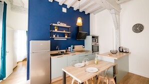 Eine kompakte Küche mit blauer Akzentwand, einer eingebauten Ablage mit Küchenutensilien, einer Mikrowelle und einem kleinen Essbereich mit Tisch und Stühlen.
