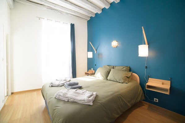 A bedroom with a bed, two bedside tables, a nightstand, a wall-mounted lamp, and a window with curtains.