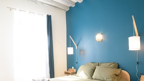 Ein Schlafzimmer mit einem Bett, einem Nachttisch, einer Wandlampe und einem Fenster mit Vorhängen.
