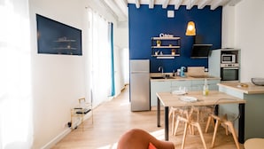 Eine moderne Küche mit blauer Akzentwand, ein Essbereich mit Holztisch und -stühlen sowie eine Küchenzeile mit Mikrowelle und Backofen.