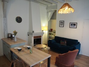 A cozy living room with a blue sofa, a wooden dining table, and a fireplace.