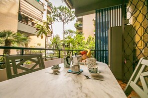 A balcony with a table set for breakfast, including a coffee pot, cups, and a fruit bowl.