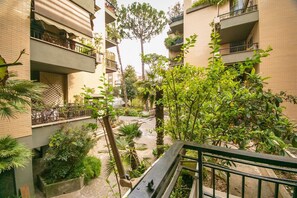 Un edificio residenziale a più piani con balconi, un cortile centrale alberato e piantumato, e una scala che conduce ai piani superiori.