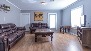 A spacious living room with a leather sofa, a wooden coffee table, and a television on a wooden stand. - Downtown sulphur getaway (Sulphur)