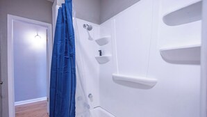 A bathroom with a bathtub, a shower, and a door leading to another room. - Downtown sulphur getaway (Sulphur)