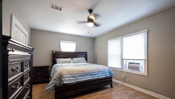 A bedroom with a dark wooden bed, a dresser, a ceiling fan, and a window with blinds. - Downtown sulphur getaway (Sulphur)