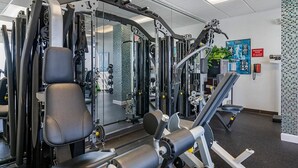 Ett gym med olika träningsmaskiner, en vägg med speglar och en affisch på väggen.