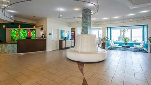 En rymlig entréhall med en receptionsdisk, en vit sittgrupp och stora fönster med utsikt över omgivningarna.