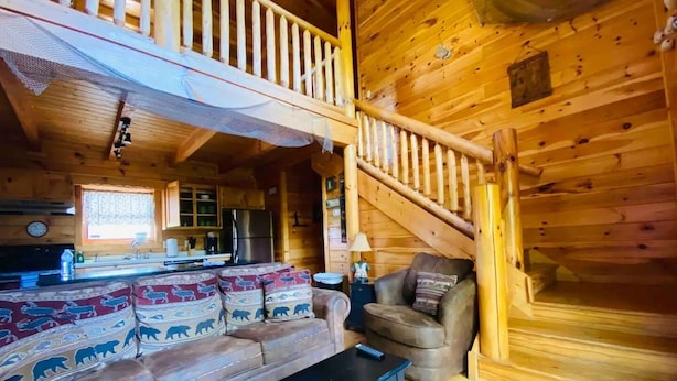 Ein Holzblockhaus-Interieur mit einer Couch, einem Sessel und einer Treppe.