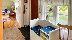 Huoneessa on valkoinen pinnasänky, puinen tuoli, pieni pöytä, jossa on lamppu, ja ikkuna, josta avautuu näkymä vehreään maisemaan.