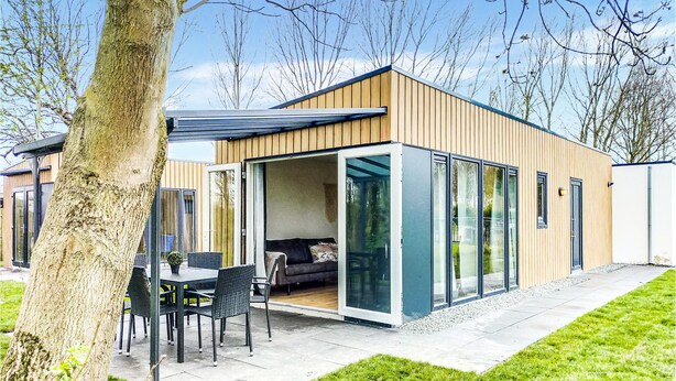 Una casa moderna de un piso con fachada de madera, puerta de cristal y un patio amueblado.