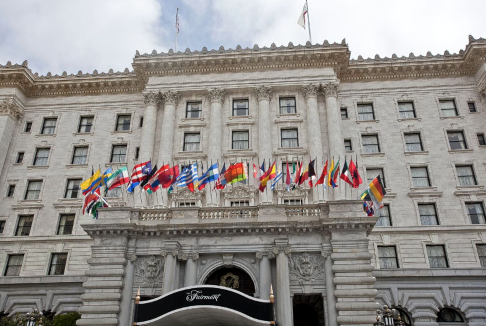 A large building with multiple flags, a prominent entrance, and a sign that reads 'Fairmont.'