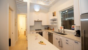 Una cucina moderna con mobili bianchi, un'isola centrale, forno integrato e frigorifero in acciaio inossidabile.