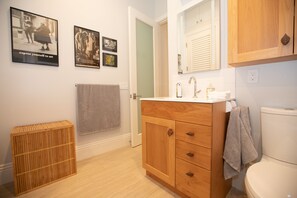 A bathroom with wooden cabinets, a white sink, and a toilet. There are two framed pictures on the wall and a wooden stool.