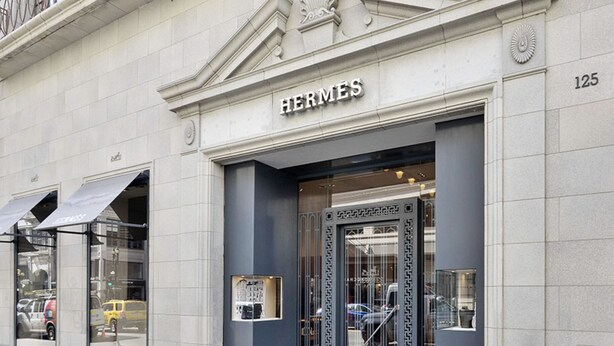 Un negozio Hermes con una facciata moderna, ampie vetrate e un ingresso ben visibile con un cancello in metallo.
