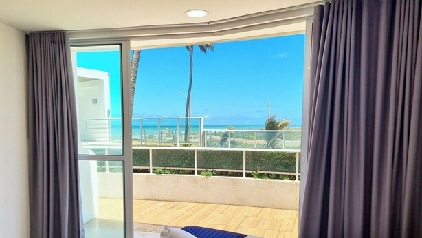 A hotel room with a bed, a view of the beach, and a balcony with a railing.