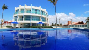 A modern hotel with a large pool, palm trees, and clear blue skies.