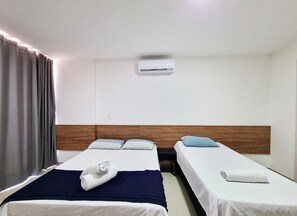 A hotel room with two single beds, a wooden headboard, an air conditioning unit, and a window with curtains. - Frente Mar com Terraço Privativo e Pet Friendly (Barra de São Miguel)