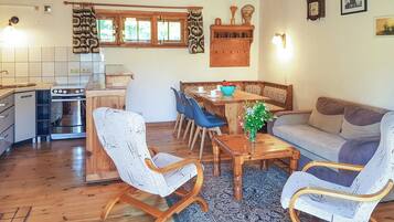 A cozy living room with a sofa, chairs, a dining table, and a kitchen area with a stove and cabinets.