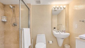 A bathroom with a glass shower enclosure, a toilet, a sink, and a mirror with lights above it.