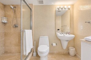 A bathroom with a glass shower enclosure, a toilet, a sink, and a mirror with lights above it.