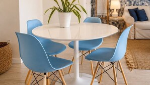 A dining area with a round table, blue chairs, a potted plant, and a patterned wallpaper background. - Walk to Beach- South of Fifth Condo | Free Parking (Miami Beach)