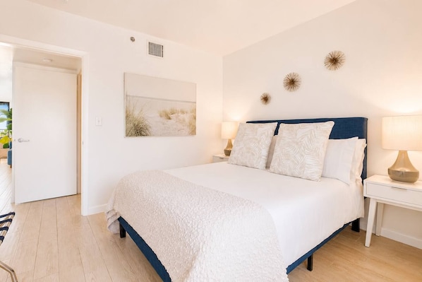 Une chambre à coucher comprenant un lit, des lampes de chevet, une œuvre d’art accrochée au mur et une porte donnant sur une autre pièce.