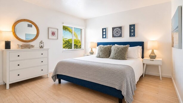 A bedroom with a bed, bedside tables, a dresser, a mirror, and wall art. - Walk to Beach- South of Fifth Condo | Free Parking (Miami Beach)