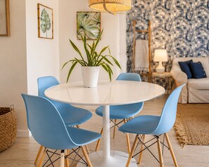 A dining area with a round table, blue chairs, a potted plant, and a patterned wallpaper background.