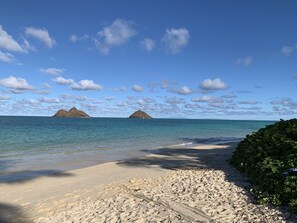 A beach with clear blue water, sandy shore, and distant mountains.