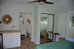 A bedroom with a bed, a ceiling fan, a dresser, a mirror, and a view of the bathroom. - Bright, upgraded house, A/C, near the ocean! CONTACT FOR RATES & AVAILABILITY! (Kailua)