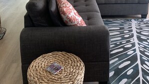Un salon moderne comprenant un canapé d’angle, un coin repas et une cuisine avec des meubles blancs et des appareils électroménagers en acier inoxydable.