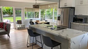 Une cuisine moderne dotée d’un îlot en marbre, d’appareils électroménagers en acier inoxydable et offrant une vue sur le jardin.