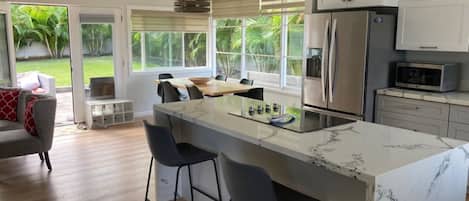A modern kitchen with a marble island, stainless steel appliances, and a view of the garden.