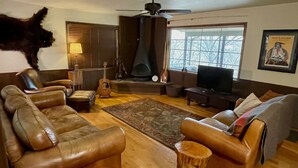 Een woonkamer met leren banken, een open haard, een televisie en een groot raam.