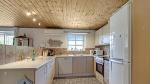 Una cucina compatta con soffitto in legno, mobili bianchi, forno a incasso e frigorifero.
