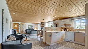 Un'ampia zona giorno con soffitto in legno, una cucina con una grande isola centrale e un'area pranzo con sedie e tavolo.