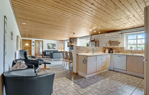 A spacious living area with a wooden ceiling, a kitchen with a large island, and a dining area with chairs and a table. - Stunning home in Ulfborg with kitchen (Ulfborg)