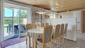 Zona pranzo con tavolo e sedie, cucina con pensili e vista su un'area salotto esterna tramite una porta vetrata.