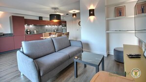 Een modern appartement met een grijze bank, een glazen salontafel, een keuken met rode kasten en een eethoek.