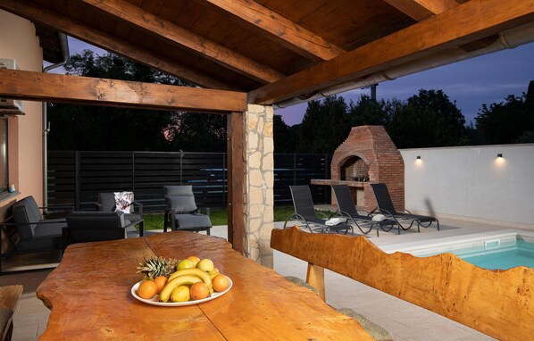 An outdoor patio with a wooden table, a fruit plate, lounge chairs, and a brick oven. - Gorgeous home in Medulin (Medulin)
