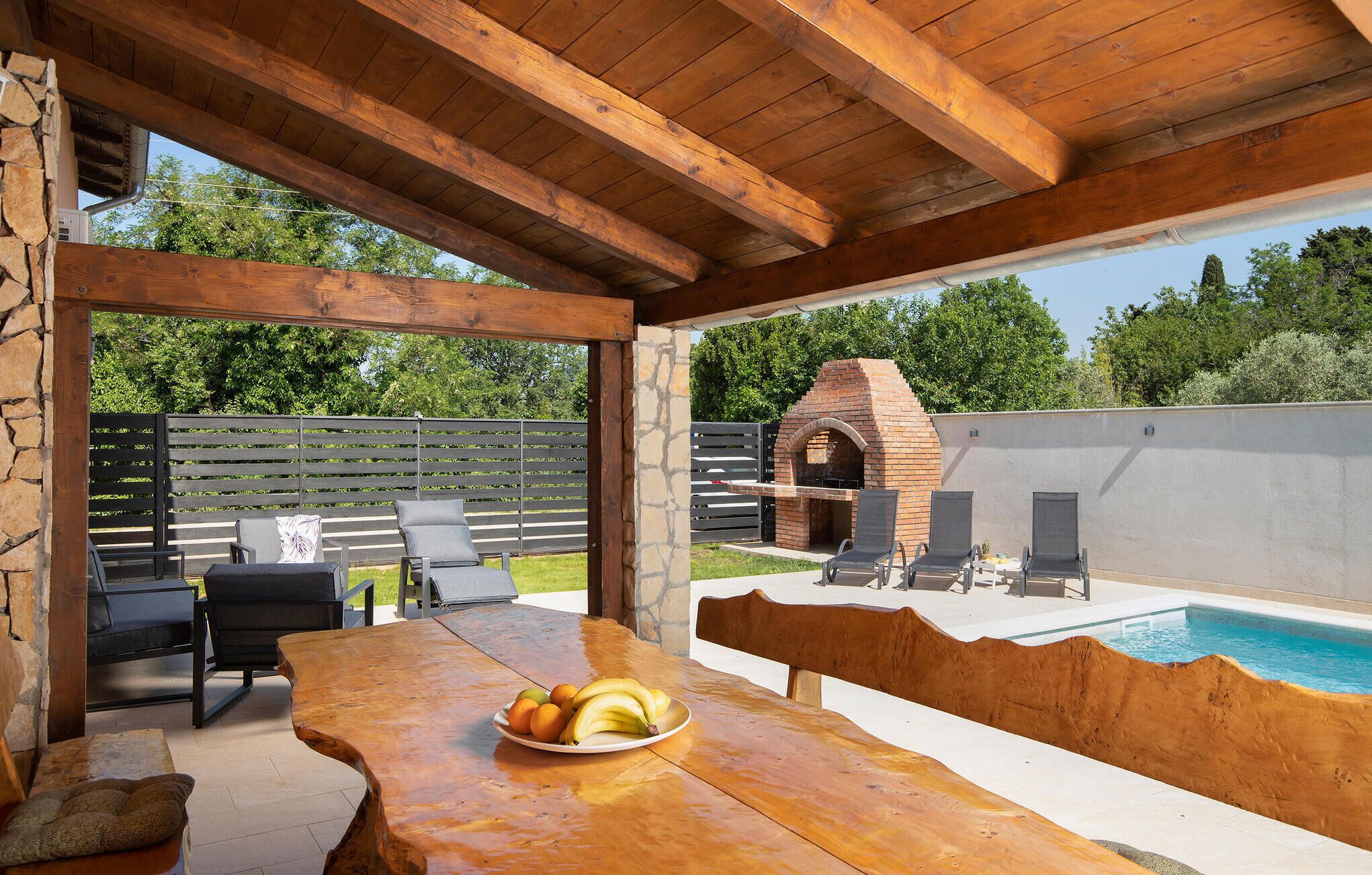 An outdoor patio with a wooden table, chairs, and a brick oven.